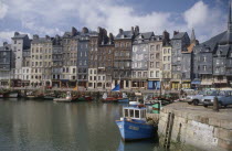 Honfleur harbour with fishing boats moored against stone quay overlooked by tall  narrow houses.