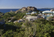 The Baths. Granite boulders amongst plants and vegetation with chairs and sun shades from a restaurants open air verandah in the middle. The ocean seen in the distance