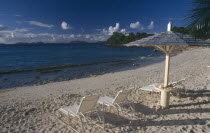 Endeavour Bay. Empty sun loungers on sandy beach with Bequia Island seen from across the sea in the distance