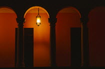 Exterior of building at night with pillars and arches and a single light illuminating an orange wall