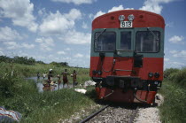Train passing people and children doing laundry in river in rural area. Zaire