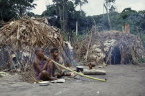 Pygmy women smoking tobacco outside thatched  domed huts. Zaire