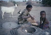 Afar tribeswoman baking bread in ground with child sitting beside her.