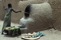 Woman making bread  cooking outside using mud brick oven.