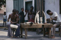 Ivory carvers working outside with watching children. Zaire