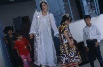 The bride wearing a white dress and silver jacket  with children around her at a village wedding.