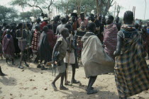 Karamojong warriors at Akuidakin ceremony to bless cattle and ask for rain.  Young girl dancing in centre is painted with Giraffe clan markings. Center