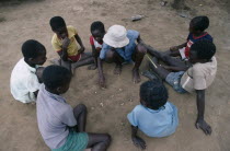 Children playing mancala game of bao using stones and depressions in ground rather than board and counters.
