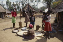 Women members of village co-operative pounding maize watched by children.co-opcooperative