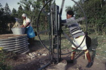 Women drawing water for washing at well.