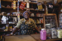 Portrait of shopkeeper behind counter with goods arranged on shelves behind her.township
