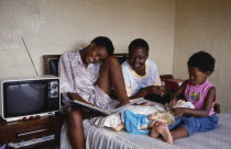 Three girls relaxing in bedroom of home.  Two eldest looking at album while youngest plays with white  blonde haired doll. domestic interiorliving