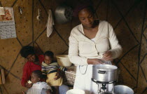 Poor family in interior of home with woman cooking over gas ring.