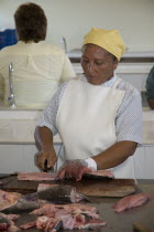 A woman wearing white apron chopping up fish. Representative of local coopera  Barranquitas