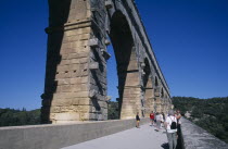 Pont du Gard Roman aqueduct.  Tourists on bridge beside arches of water channel above.