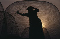Fisherman mending net silhouetted against sunset sky. United Arab Emirates