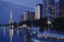 Modern high rise buildings and the Eiffel Tower from the banks of the River Seine illuminated at dusk.