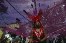 Notting Hill Carnival  dancer in pink and red costume following a float.
