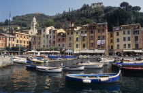 Harbour with moored boats and pastel coloured waterside houses  tree covered hillside behind. Colored