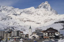 Ski resort town with church  hotel and petrol pumps with snow covered peak of the Matterhorn behind.Gasoline  Monte Cervino