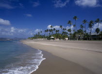 Four Seasons Resort.  Quiet sandy beach at the waters edge.  Line of empty sun loungers with apartment buildings partly seen through palm trees behind.