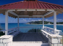 Wooden decking with red painted roof and white seating framing view out over the bay and beach.