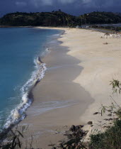View along quiet sandy beach and bay with a few people sunbathing with road towards tree covered headland behind.