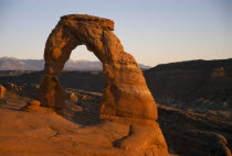 Delicate Arch. Free standing  red cresent of rock at canyon edge. Mountainous landscape beyond.