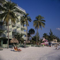 Hotels next to sandy beach lined with palm trees and sunbathers on the sand