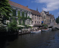 Boats dock on the canal near a bridge  next to an ivy covered building with canopies.