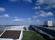 Seven Mile Bridge. Commemorative plaque with the Honorable Florida State Representative Bernie C Papy seen in the foreground with a truck driving along the concrete bridge stretching out over the sea...