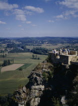 Domme. People standing on a brick platform on a rocky hill looking over the green landscape.