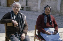 Two elderly women sitting on chairs in street