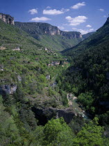 Sainte Enimie.  View along the Gorges du Tarn towards village set on steep hillside and tree covered rocky hills behind.