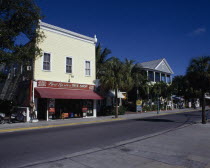 View across an empty street lined with shopfronts including a Diving shop with palm trees and blue sky