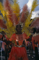 Notting Hill Carnival. Woman in orange costume with orange and yellow feathers and gold head-dress.