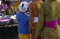 Cropped view from behind of young boy in traditional dress standing beside two smartly dressed women.
