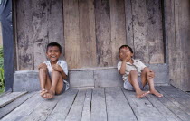 Two laughing children sitting on wooden floor of building.