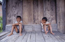 Two laughing children sitting on wooden floor of building.