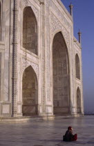 Taj Mahal.  Part view of white marble exterior with woman sitting on polished floor in foreground.