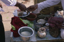 Cropped shot of paan seller making transaction with customer across stall with paan leaves and other ingredients.
