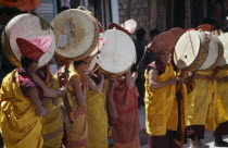 Tibetan Buddhist lamas in ceremonial dress playing traditional drums supported on poles at the commencement of a festival.rGna