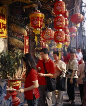 Wat Traimit.  People offering prayers and incense at temple decorated with red Chinese lanterns and strings of coloured lights for Chinese New Year.Colored