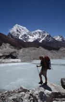 Person standing on outcrop looking over glacial lake with snow covered mountain peaks beyond on Everest Base Camp trek.