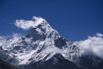 Mount Ama Dablam.  Snow covered peak of west face in drifting cloud against blue sky in May.6856 m