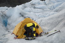 Mountaineer attaching crampons to his boots in front of tent set up in a crevasse.Trek from Glacier Chico  Chile  to El Chalten  Argentina