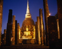 Colonnade leading to massive seated Buddha and stupa illuminated at dusk during Loi Krathong festival of lights.