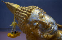 Head of reclining Buddha with gold leaf and floral offering.