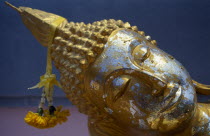 Head of reclining Buddha with gold leaf and floral offering.