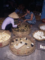 Female vendor selling eggs  chicks and ducklings in market with customer selecting ducklings.